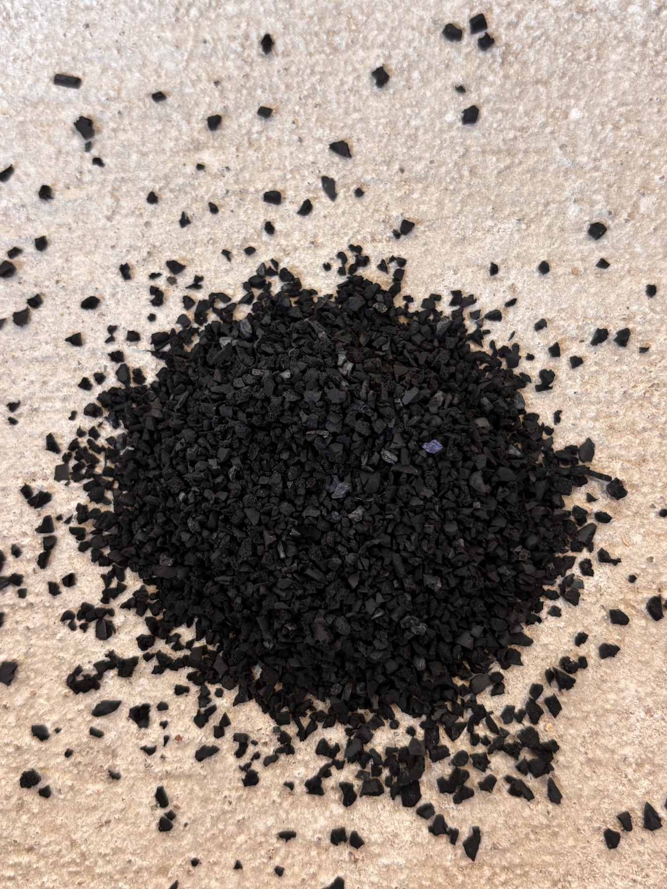 Close-up of black recycled rubber granules showing their irregular texture.